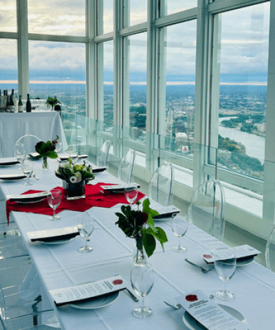 Long dinner table set with white linen and a red runner beside floor-to-ceiling windows overlooking Boston at View Boston